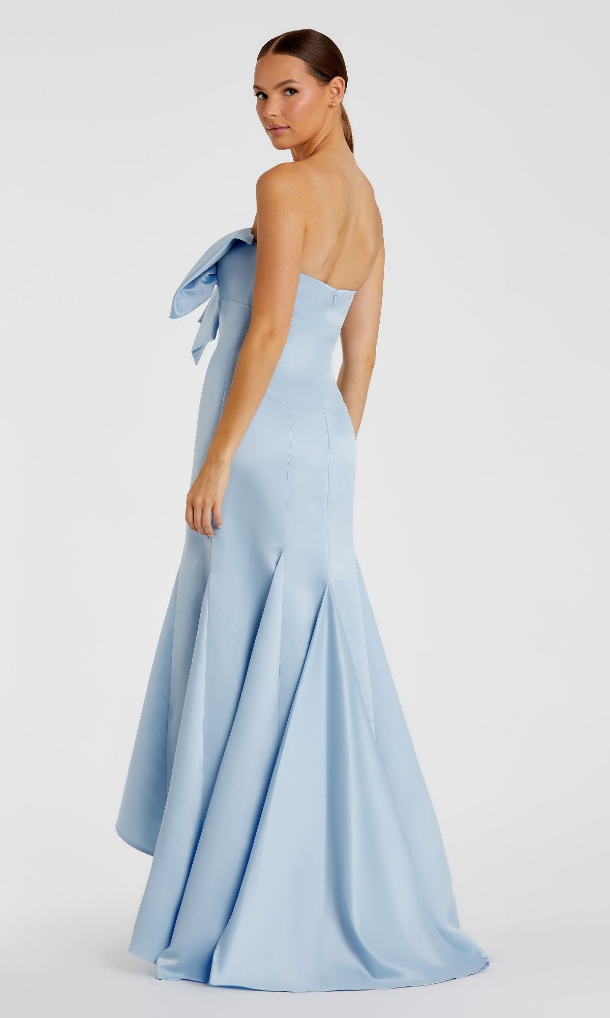 A woman models the Mac Duggal 49701, a light blue strapless mermaid formal dress with a large bow on the bodice, floor-length, standing against a plain white background.